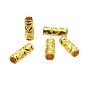 Puede incluir: Cinco cuentas de metal de color dorado con un patr&oacute;n geom&eacute;trico. Las cuentas son cil&iacute;ndricas y tienen un acabado liso y brillante.