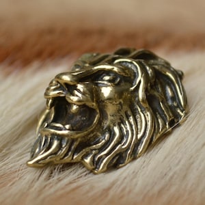 以下が含まれることがあります： 獰猛な表情をした、精巧な真鍮製のライオンの頭部の彫刻。ライオンのたてがみは複雑に彫刻されており、頭部は右を向いている。