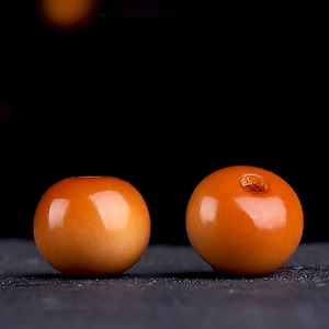 以下が含まれることがあります： 中央に小さな穴が開いた、滑らかで丸いオレンジ色のビーズが2つ。ビーズは木でできており、光沢のある仕上げになっています。