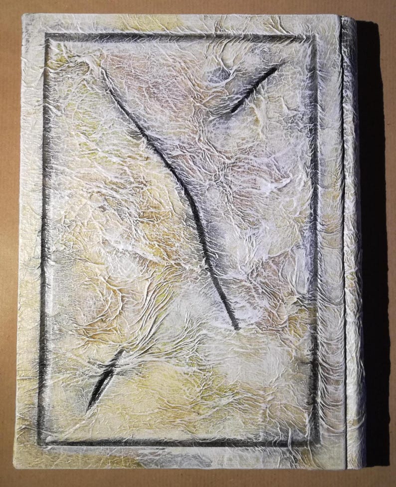 Op de afbeelding: Getextureerd rechthoekig kunstwerk met een cr&egrave;me- en gele achtergrond, omlijst door een donkergrijze rand. Een zwart, abstract ontwerp verdeelt het midden. Het oppervlak heeft een gerimpeld, gelaagd uiterlijk.