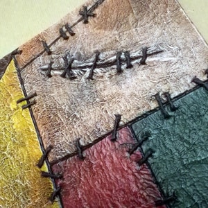 May include: A handmade journal with a patchwork cover. The cover is made of different colored leather pieces, including brown, yellow, red, and green. The pieces are sewn together with brown thread. The journal has a distressed, vintage look.