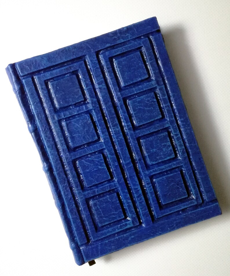 May include: A blue leather-bound journal with a raised design of a square pattern, resembling a door.