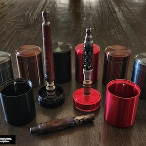 May include: A collection of seven metal containers with various finishes, including silver, black, red, and copper.  The containers are cylindrical and have a screw-on lid.  Two wooden vape pens are also included in the image.  Picture For Display Purposes Only. Items Included in Description.
