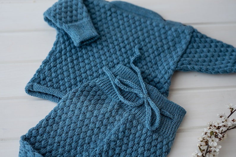 Op de afbeelding: Een blauwe gebreide babytrui en broekset met een textuurpatroon. De set is gemaakt van zacht garen en heeft een comfortabele pasvorm.
