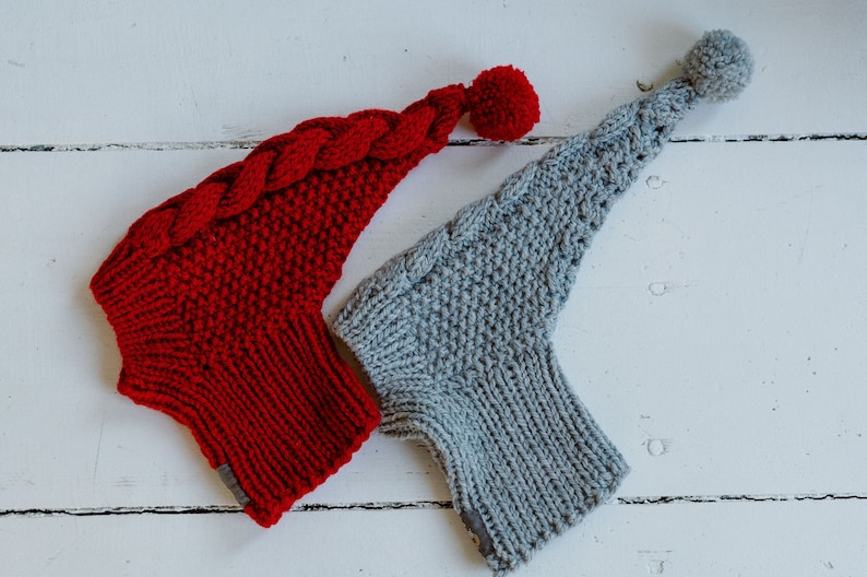 May include: Two knitted hats with pom-poms. One hat is red with a braided detail and the other is gray.