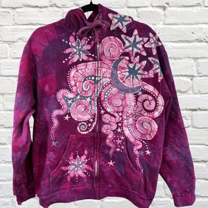 Può includere: Una felpa con cappuccio con zip tie-dye viola con un design celeste. Il design presenta una luna crescente, stelle e motivi a spirale nelle tonalità del rosa e del viola. La felpa con cappuccio ha un cappuccio con coulisse e due tasche anteriori.