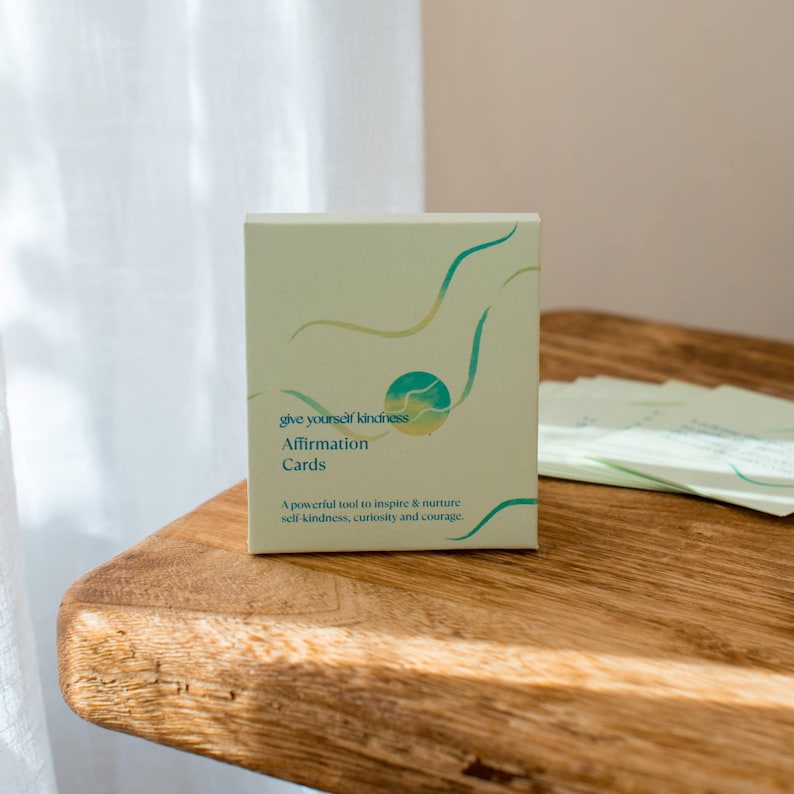 May include: A box of green and yellow affirmation cards with the text "give yourself kindness Affirmation Cards" and "A powerful tool to inspire & nurture self-kindness, curiosity and courage."