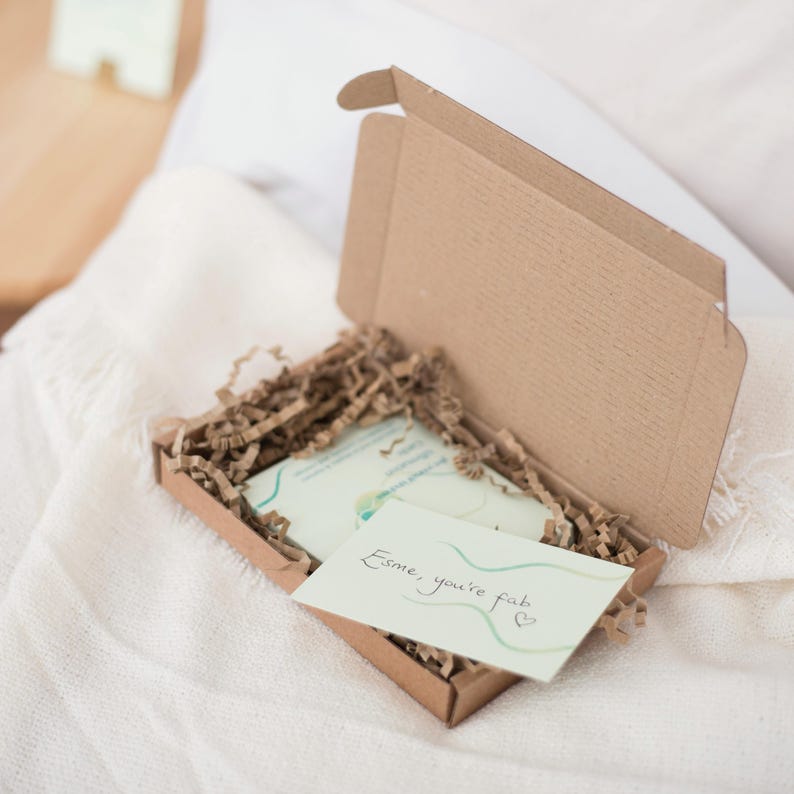May include: A small cardboard box with a handwritten note inside that says "Esme, you're fab." The box is filled with brown packing paper.