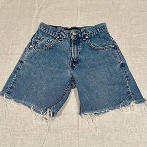 May include: A pair of light blue denim shorts with frayed edges. The shorts have a classic five-pocket design and a button fly.