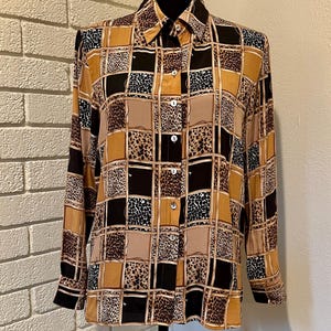 Puede incluir: Camisa abotonada de manga larga con un estampado geométrico. La camisa presenta una mezcla de cuadrados beige, negros y marrones, algunos con estampado de leopardo. La camisa se exhibe en un maniquí negro.