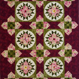 May include: A rectangular quilt featuring a deep burgundy background with a repeating pattern of six circular blocks containing star motifs. The stars are composed of pink floral fabric and dark green triangles, surrounded by green and pink floral squares.