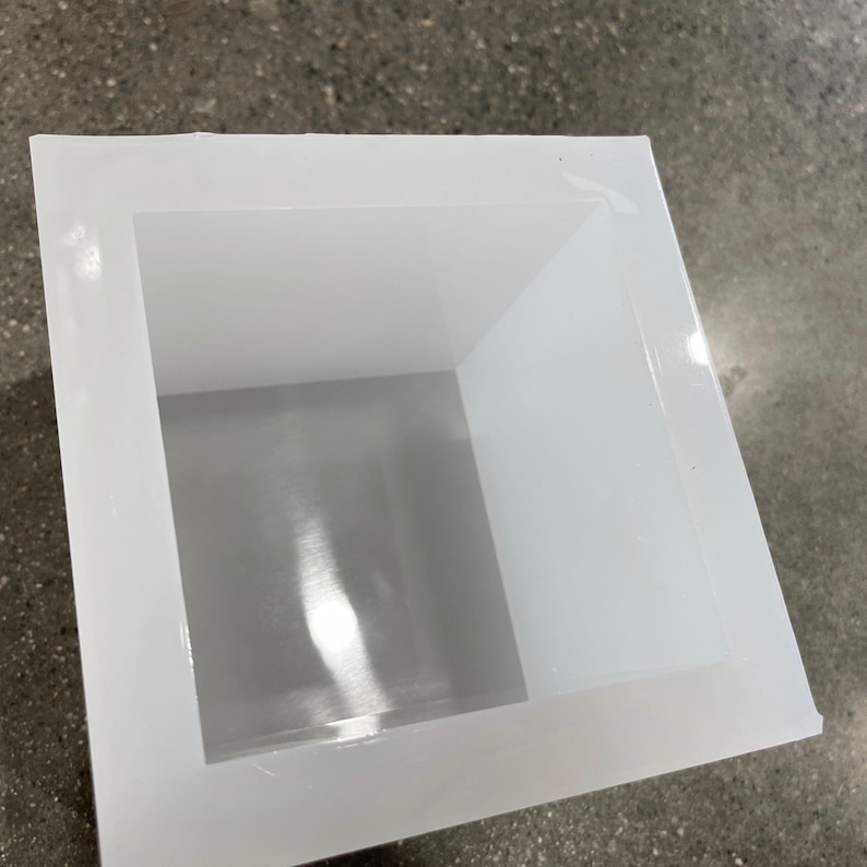 May include: A white silicone mold for making soap or other crafts. The mold is square and has a smooth, glossy finish.
