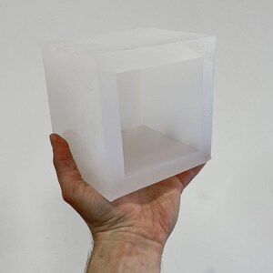 May include: A clear, translucent, cube-shaped silicone mold with a square opening in the center.