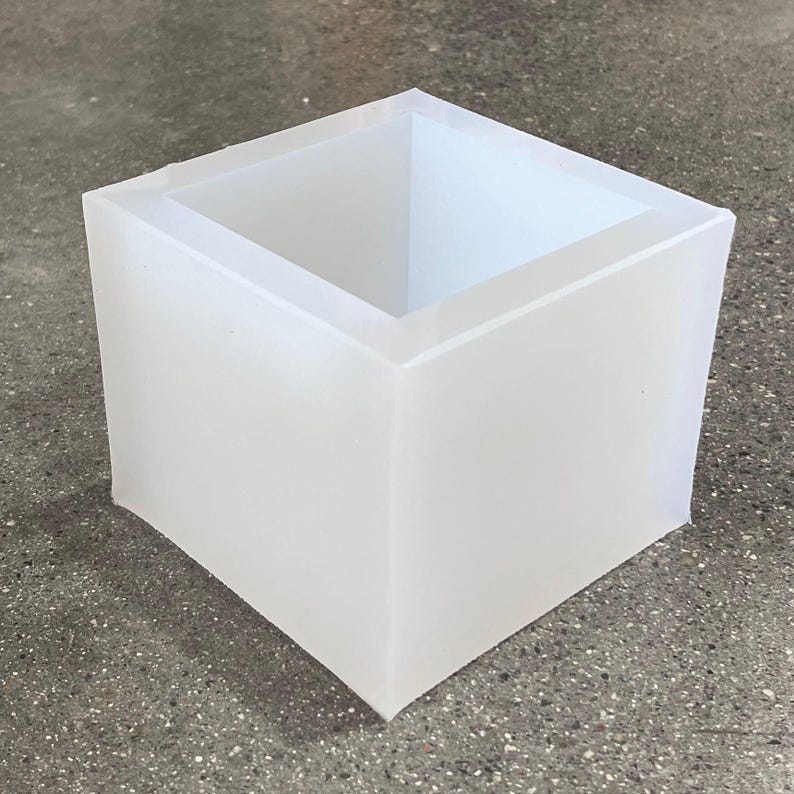 May include: A white square silicone mold for making candles or soap. The mold is made of flexible silicone and has a smooth, glossy finish.