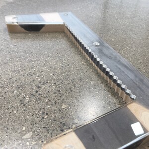 May include: A wooden and metal L-shaped tool with a serrated edge. The tool has a black and white striped pattern on the wood.