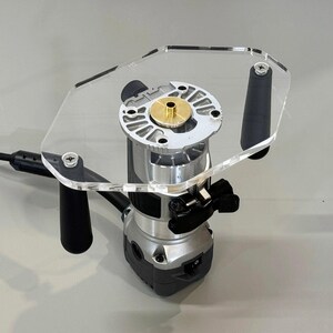 May include: A clear acrylic router table with a black router attached. The router has a brass insert and a black on/off switch.
