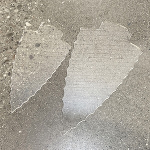 May include: Two clear plastic pieces with a wavy edge, laid out on a gray concrete surface.