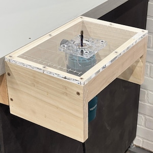 May include: A wooden router table with a clear acrylic top and a router bit fitted. The router is attached to the table and is ready for use.