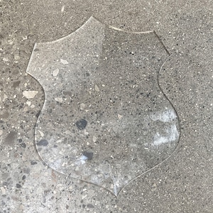 May include: A clear plastic shield shape on a gray concrete background.