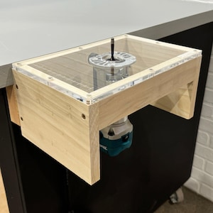 May include: A wooden router table with a clear acrylic top and a teal-colored router attached underneath. The router table is mounted to a workbench.