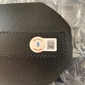 May include: A black leather item with a Beckett Witnessed sticker and a barcode sticker with the number 1W281591.