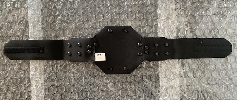 May include: Black leather wrestling championship belt with a large octagonal center plate and metal studs. The belt has a velcro closure and the text "WWE" is printed on the center plate.