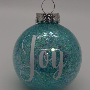 May include: A teal blue Christmas ornament with glitter and the word "Joy" in white lettering.