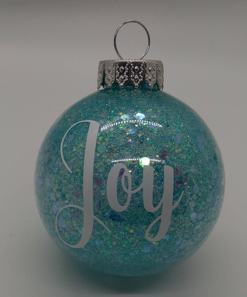 May include: A teal blue Christmas ornament with glitter and the word "Joy" in white lettering.