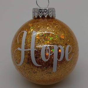 May include: Gold glitter Christmas ornament with the word "Hope" in white lettering.