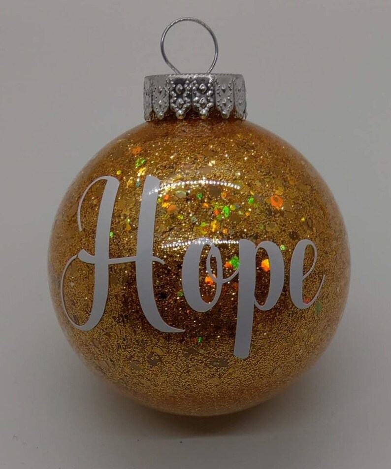 May include: Gold glitter Christmas ornament with the word "Hope" in white lettering.