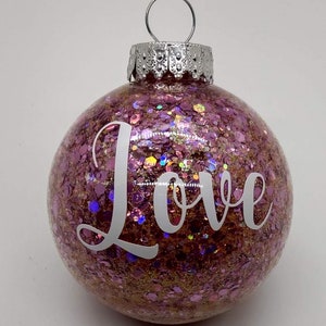 May include: Pink Christmas ornament with glitter and the word "Love" in white lettering.