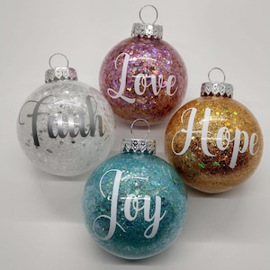 May include: Four glittery Christmas ornaments with the words "Faith", "Love", "Hope", and "Joy" written in white on each ornament.