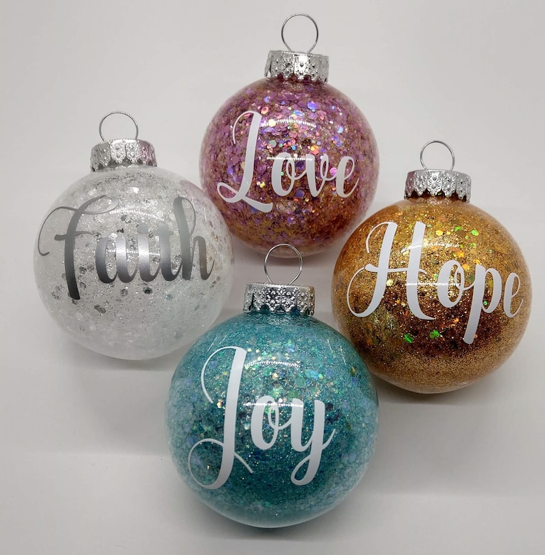May include: Four glittery Christmas ornaments with the words "Faith", "Love", "Hope", and "Joy" written in white on each ornament.