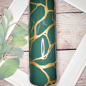 May include: A green and gold tumbler with a gold leaf pattern. The tumbler is made of stainless steel and has a double-walled design.