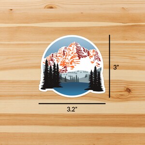 May include: A 3 inch round sticker featuring a mountain range with snow-capped peaks, a blue lake, and a forest of evergreen trees. The sticker is printed on white vinyl with a glossy finish.