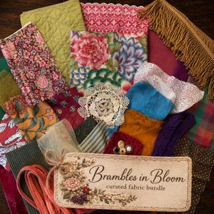 May include: A collection of assorted fabric scraps featuring floral, quilted, and patterned textiles in various colors, including gold fringe trim, a white lace doily, and a rectangular tag labeled Brambles in Bloom curated fabric bundle.