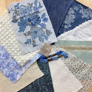 May include: A collection of fabric swatches including blue and white floral prints, solid dark blue denim, white textured dot fabric, a light green striped piece, a cream crochet square, and two skeins of blue embroidery floss with two needles.