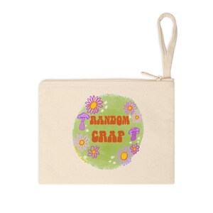 May include: A white canvas zippered pouch with a green circle design featuring the text "RANDOM CRAP" in orange. The circle is surrounded by purple and yellow flowers and mushrooms.