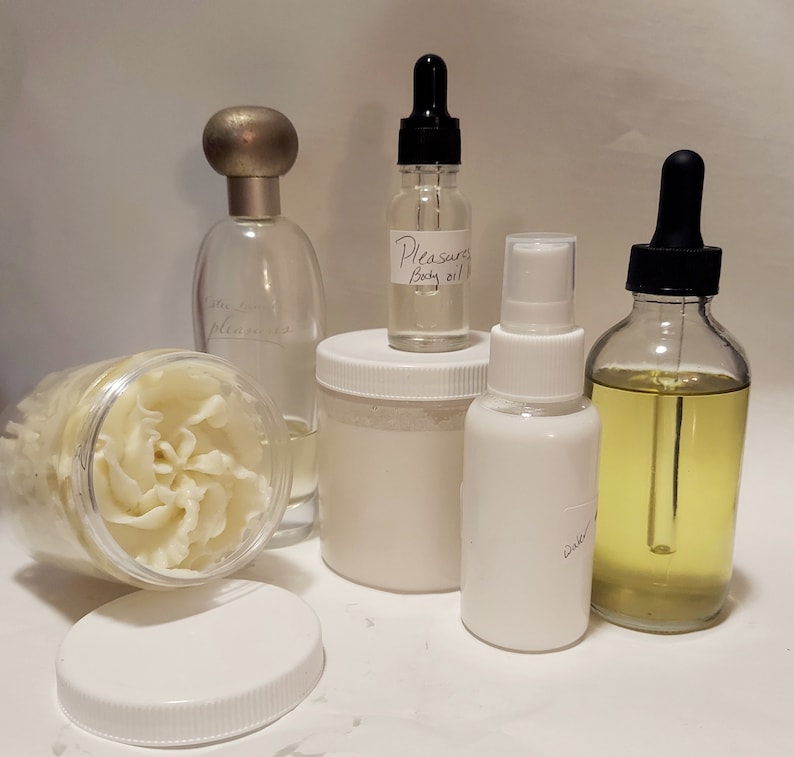 Puede incluir: Una colecci&oacute;n de cinco productos de cuidado personal, que incluye una botella de vidrio transparente con una tapa plateada etiquetada como "extra pleasure", una botella de vidrio transparente con un gotero negro y una etiqueta blanca que dice "Pleasure Body Oil", un frasco blanco con una tapa blanca, una botella blanca con una boquilla de pulverizaci&oacute;n etiquetada como "Water", y una botella de vidrio transparente con un gotero negro y un l&iacute;quido amarillo.