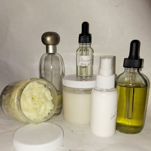 Puede incluir: Una colecci&oacute;n de productos para el cuidado del cuerpo que incluye un tarro blanco de manteca corporal, una botella de vidrio transparente de aceite corporal etiquetada como "Pleasure Body Oil", una botella blanca de loci&oacute;n a base de agua, una botella de vidrio transparente de perfume y una botella de vidrio transparente de aceite con gotero.