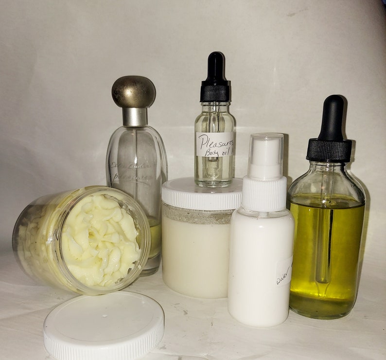 Puede incluir: Una colecci&oacute;n de productos para el cuidado del cuerpo que incluye un tarro blanco de manteca corporal, una botella de vidrio transparente de aceite corporal etiquetada como "Pleasure Body Oil", una botella blanca de loci&oacute;n a base de agua, una botella de vidrio transparente de perfume y una botella de vidrio transparente de aceite con gotero.