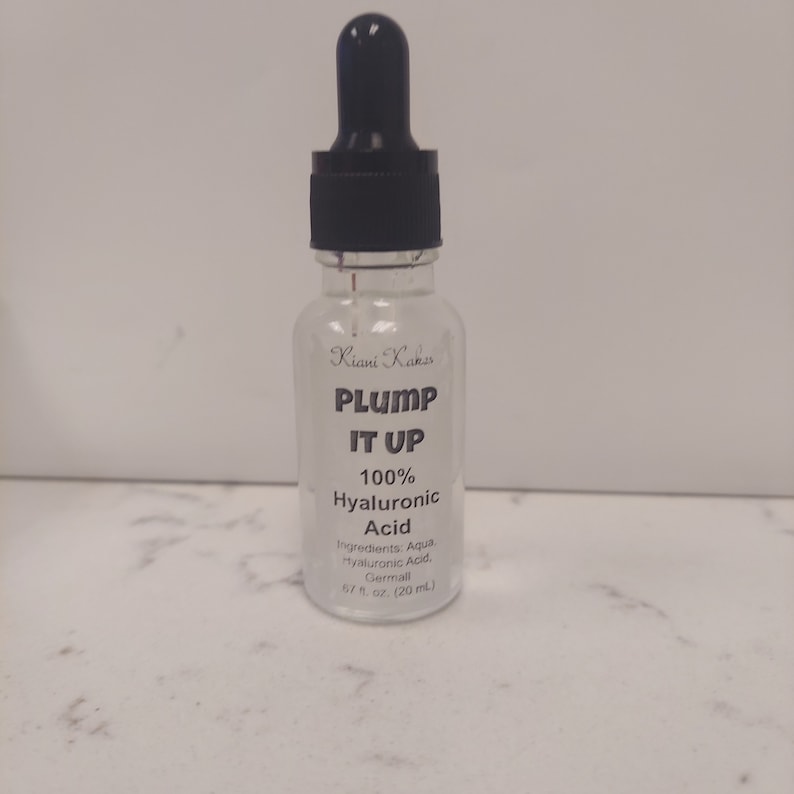 Może przedstawiać: Przezroczysta szklana butelka z czarną pipetą. Butelka jest oznaczona etykietą "Kiani Kaks PLUMP IT UP 100% Hyaluronic Acid" i "Składniki: Aqua Hyaluronic Acid. Germall 67 fl oz (20 ml)".