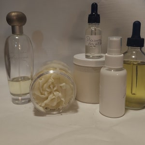 Puede incluir: Una colecci&oacute;n de productos para el ba&ntilde;o y el cuerpo que incluye una botella de vidrio transparente de aceite corporal etiquetada como "Pleasures Body Oil 1 oz", un tarro blanco de manteca corporal, una botella de vidrio transparente de perfume, una botella blanca de spray corporal y una botella de vidrio transparente de aceite.