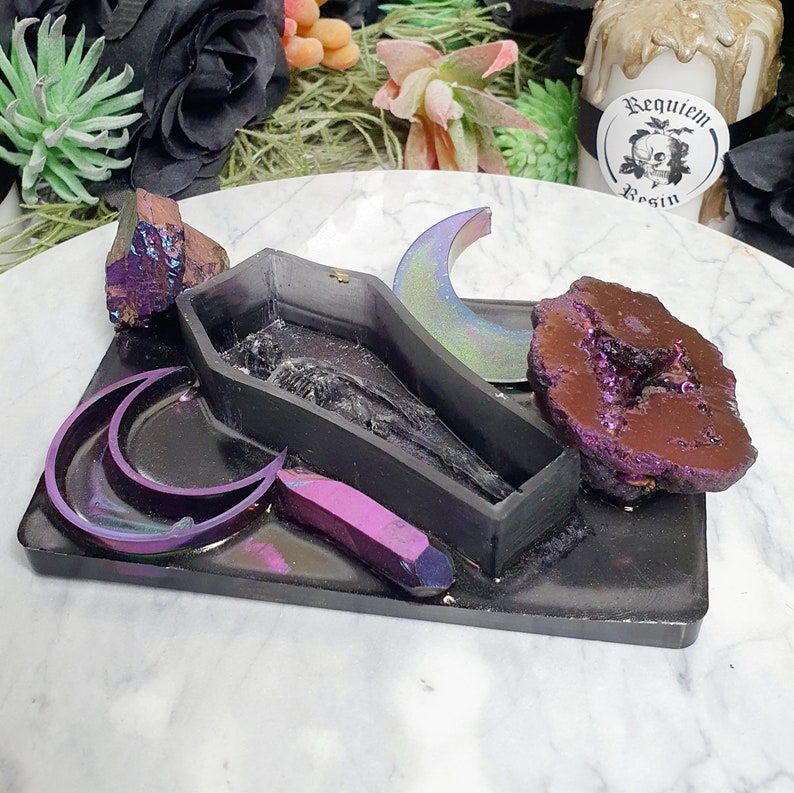 May include: A black resin tray with a coffin-shaped mold, two crescent moon molds, a purple crystal, and a large purple geode. The tray is decorated with iridescent glitter.