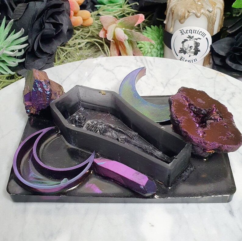 May include: A black resin tray with a coffin-shaped mold, two crescent moon molds, a purple crystal, and a large amethyst geode. The tray is decorated with iridescent glitter.