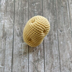 May include: A crocheted, light brown, potato-shaped toy. The toy is sitting on a wooden surface.