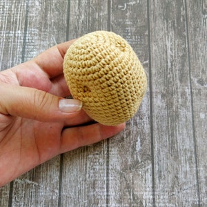 May include: A close-up of a crocheted brown ball, held in a hand. The ball is made of yarn and has a textured surface.
