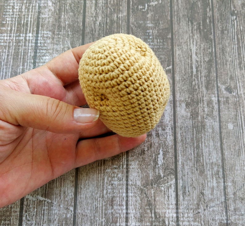 May include: A close-up of a crocheted brown ball, held in a hand. The ball is made of yarn and has a textured surface.