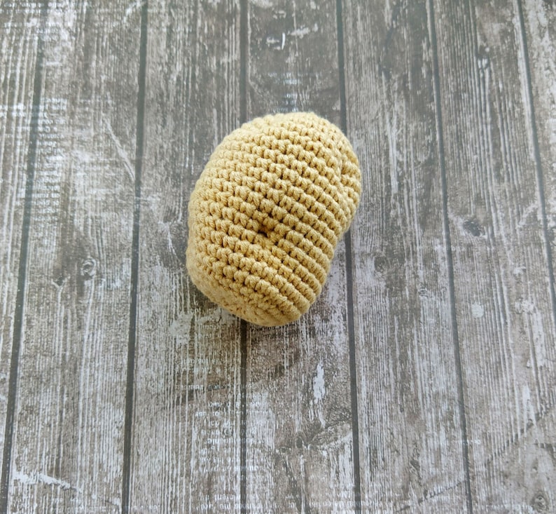 May include: A beige crocheted beanie hat on a woodgrain background.