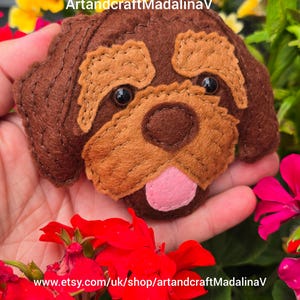 May include: A handcrafted felt dog head in brown and tan, featuring black bead eyes and a pink tongue. The Etsy shop name "ArtandcraftMadalinaV" and the shop's URL are visible in the image.